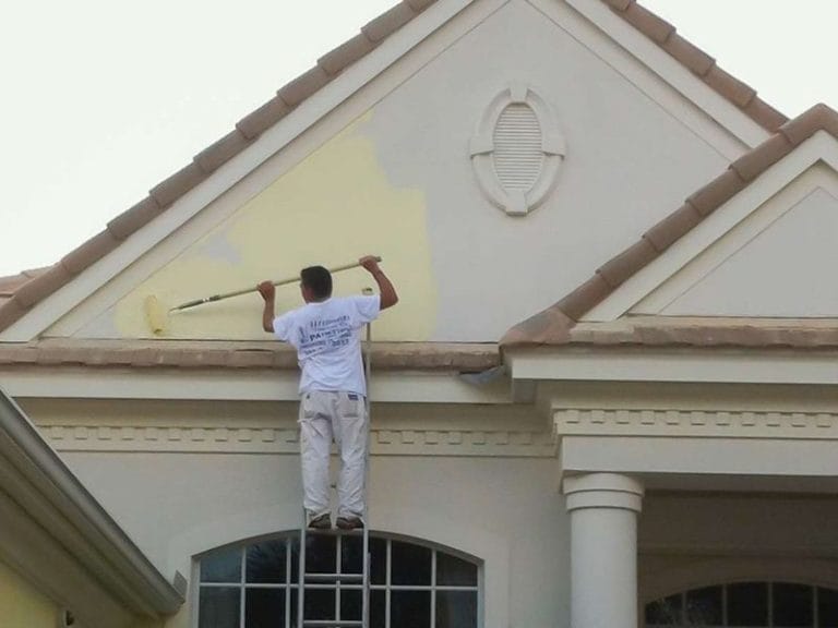 Guy Painting a House on Ladder with Paint Roller