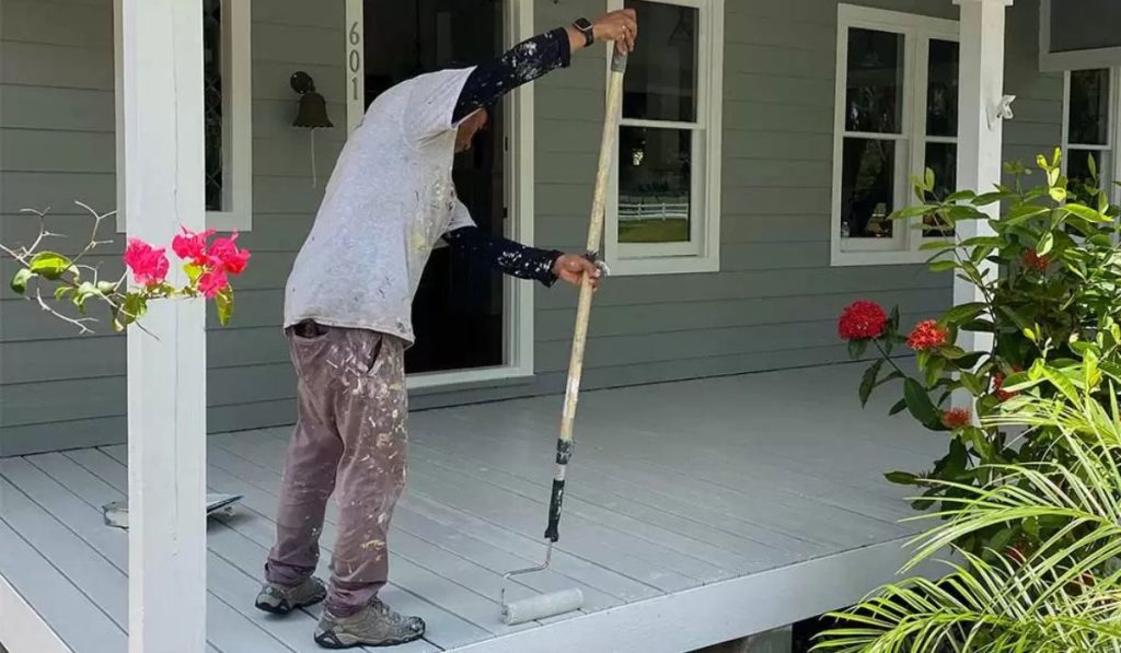 Licensed painting contractor from Ultimate Services Co. rolling a fresh coat of paint on a front porch deck at a Sarasota home