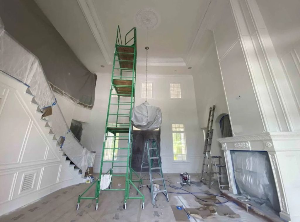 Ultimate Services Co. painting crew on scaffolding completing a high-ceiling interior painting project in a Sarasota home with detailed wainscoting and crown molding